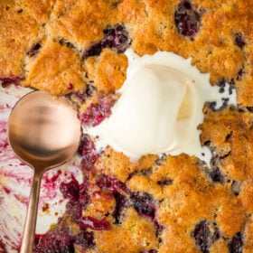 a blackberry cobbler with a serving missing and a scoop of vanilla ice cream in the middle.
