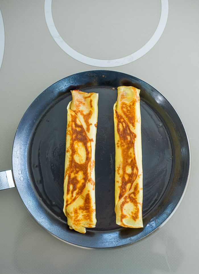 two crispy rolled pizza crepes in an oiled pan.