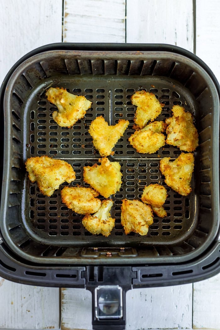 cooked and battered cauliflower in an air fryer basket.