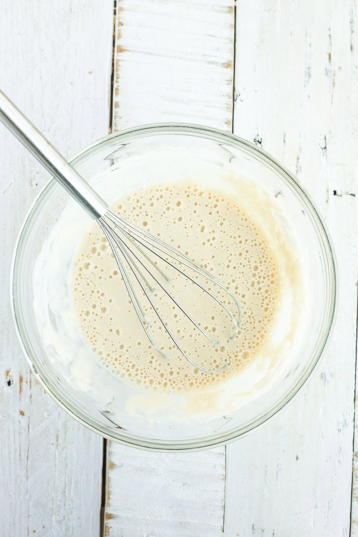 a flour batter in a glass bowl with a whisk in it.