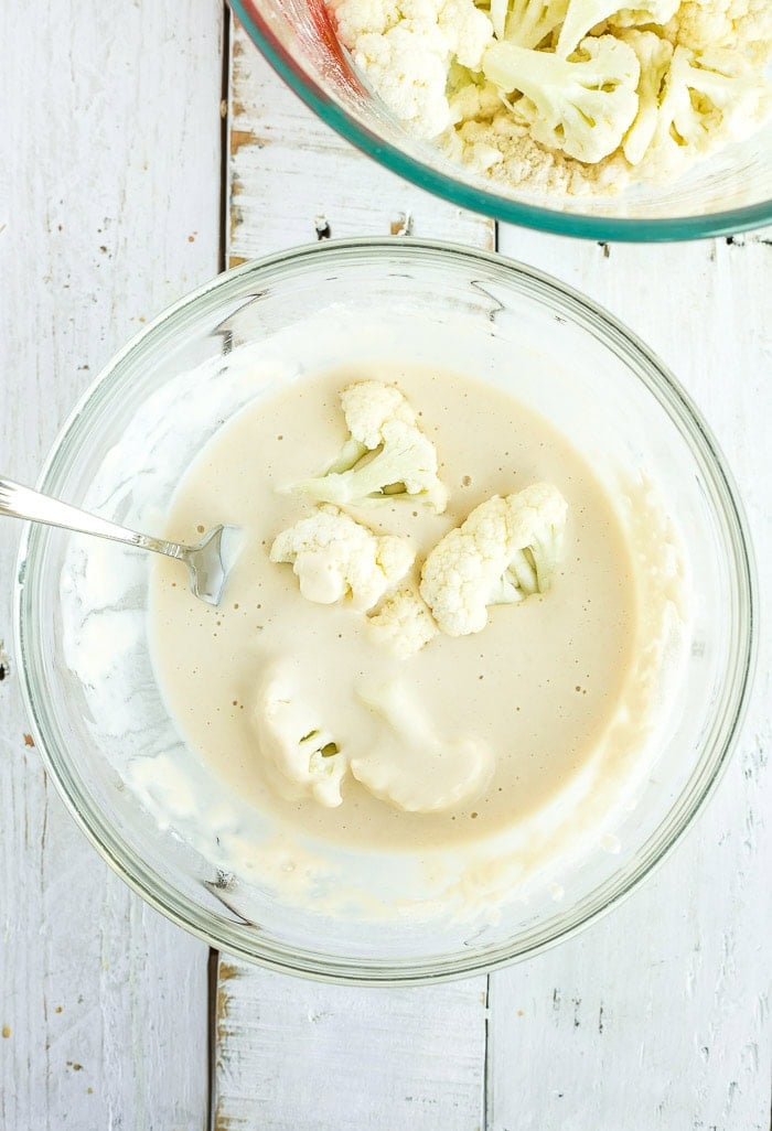 cauliflower florets in a glass bowl of batter.