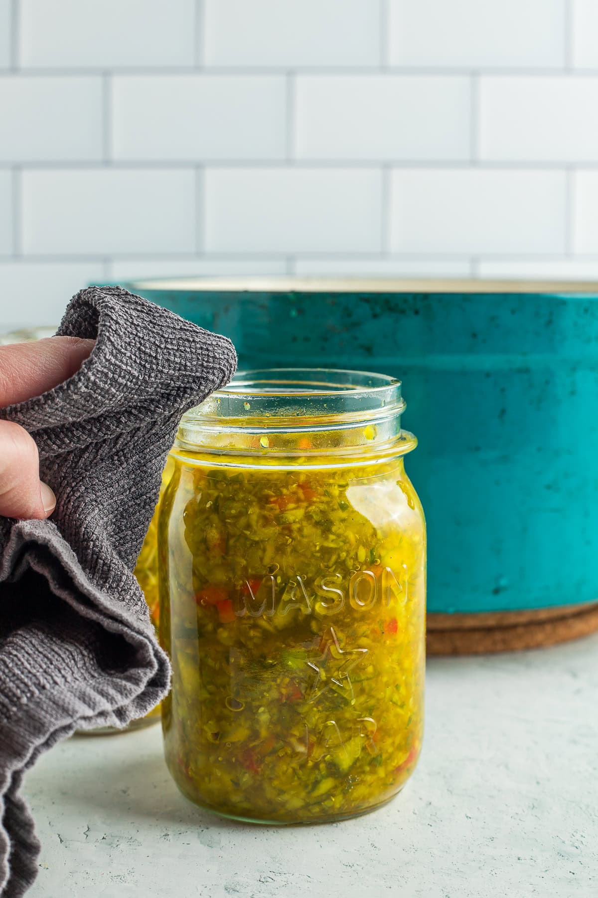 a hand with a grey rag wiping a canning jar rim.