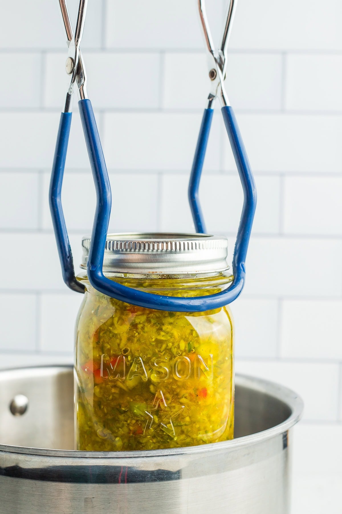canning tongs lowering a jar into a saucepan.