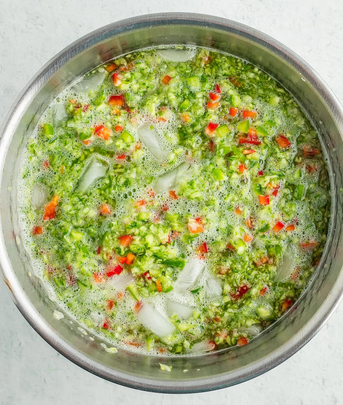 chopped vegetables in a metal bowl with ice cubes.