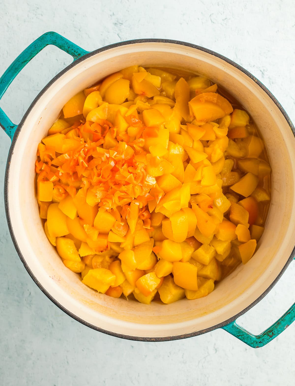 chopped peaches and peppers in a teal dutch oven.