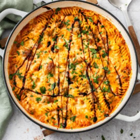 bruschetta chicken casserole in a white braiser dish with balsamic reduction drizzled on top and chopped basil.