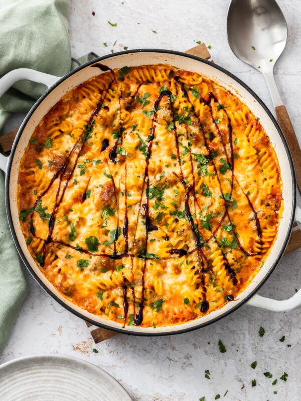 bruschetta chicken casserole in a white braiser dish with balsamic reduction drizzled on top and chopped basil.