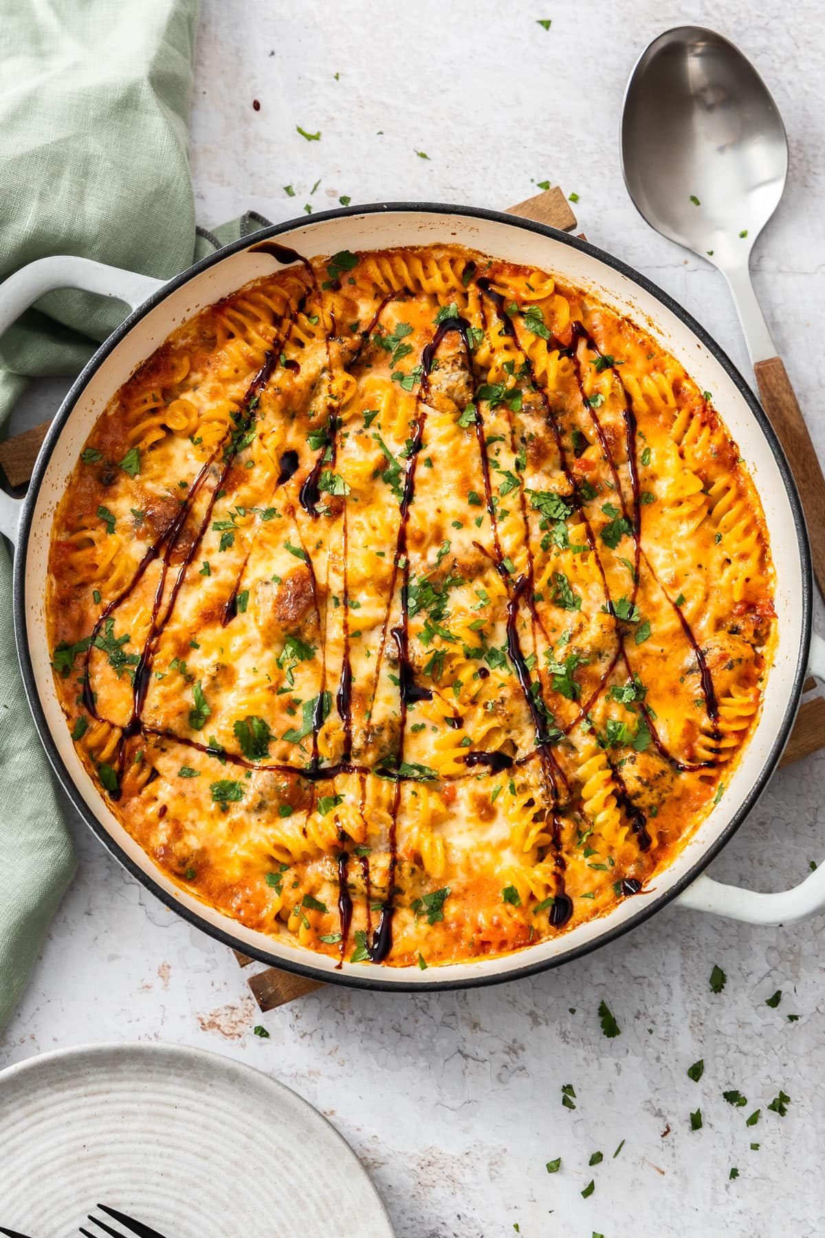 bruschetta chicken casserole in a white braiser dish with balsamic reduction drizzled on top and chopped basil.