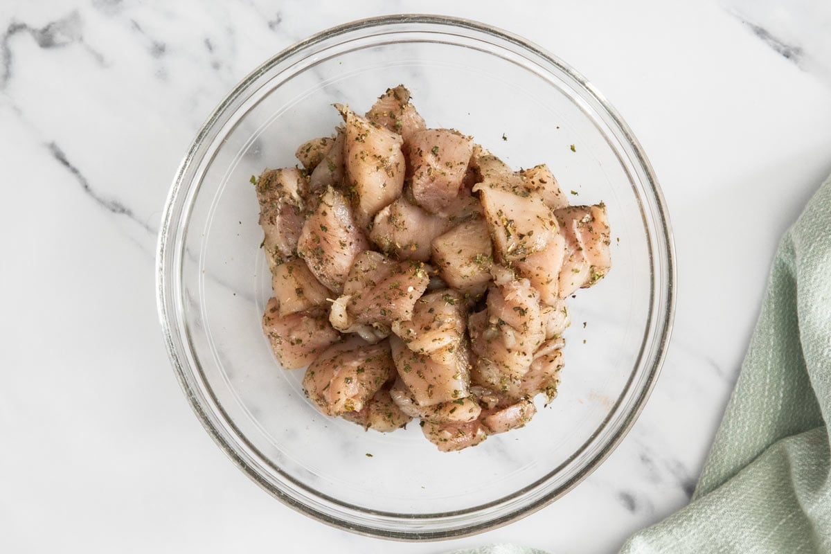 uncooked chicken with herbs in a glass bowl.