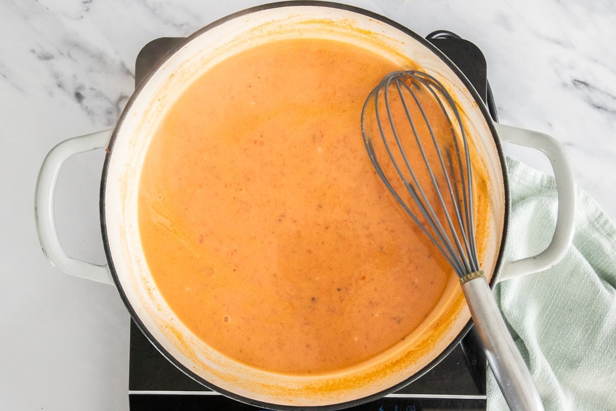 a whisk in a white skillet with a creamy tomato sauce.