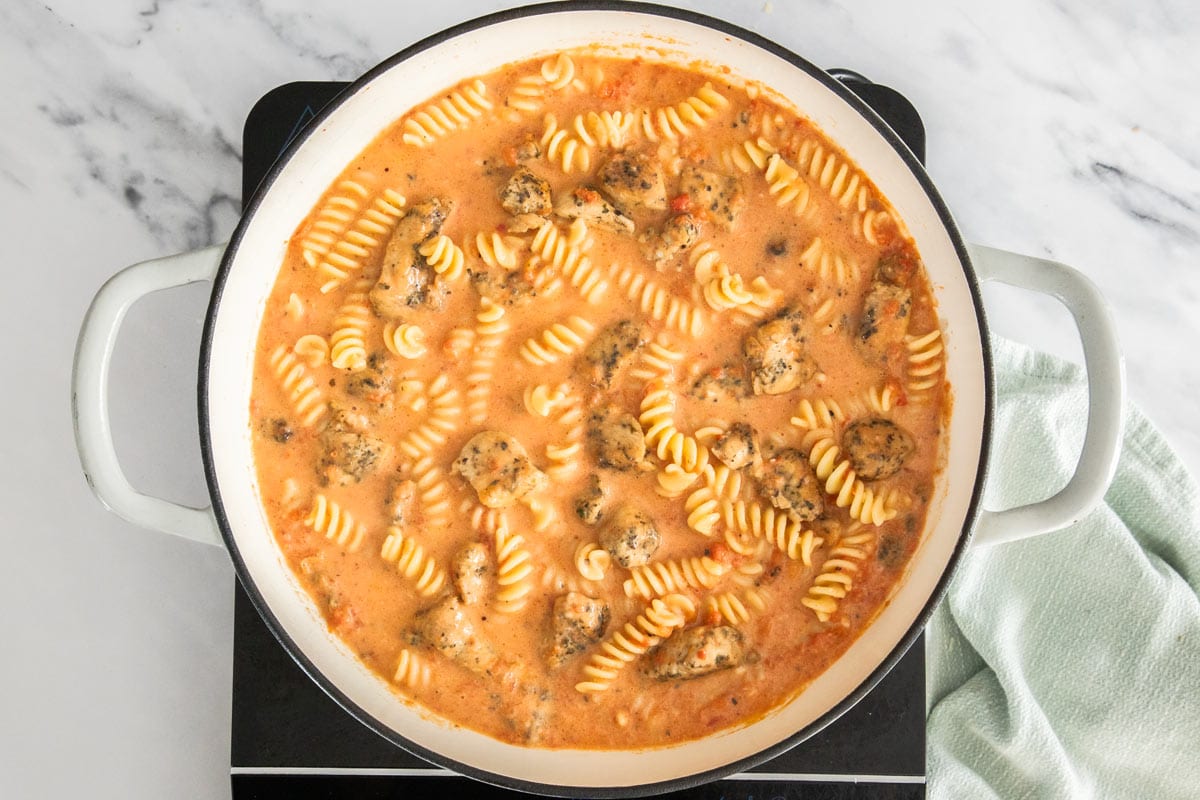 pasta and chicken in a white skillet with a creamy tomato sauce.