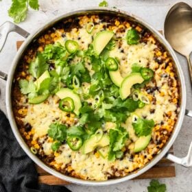 a taco-flavored beef and rice skillet topped with melted cheese, cilantro, green onions, and avocado.