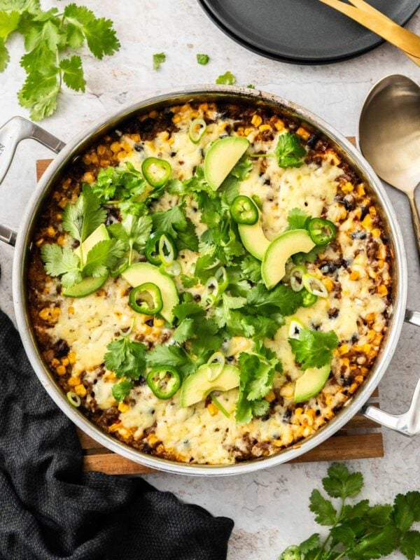 a taco-flavored beef and rice skillet topped with melted cheese, cilantro, green onions, and avocado.