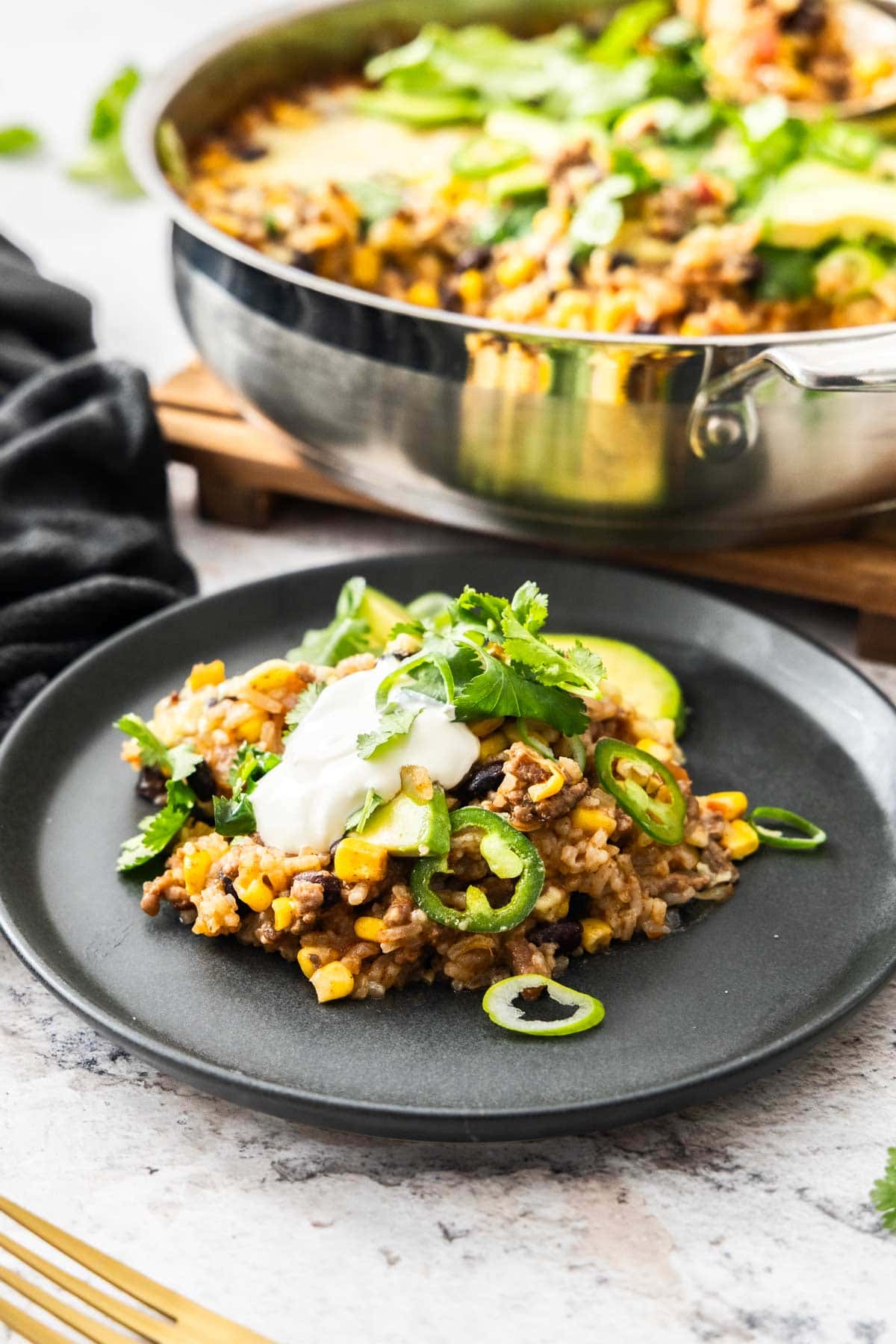 a serving of taco flavored casserole on a grey plate topped with sour cream, cilantro, and jalapeno slices.