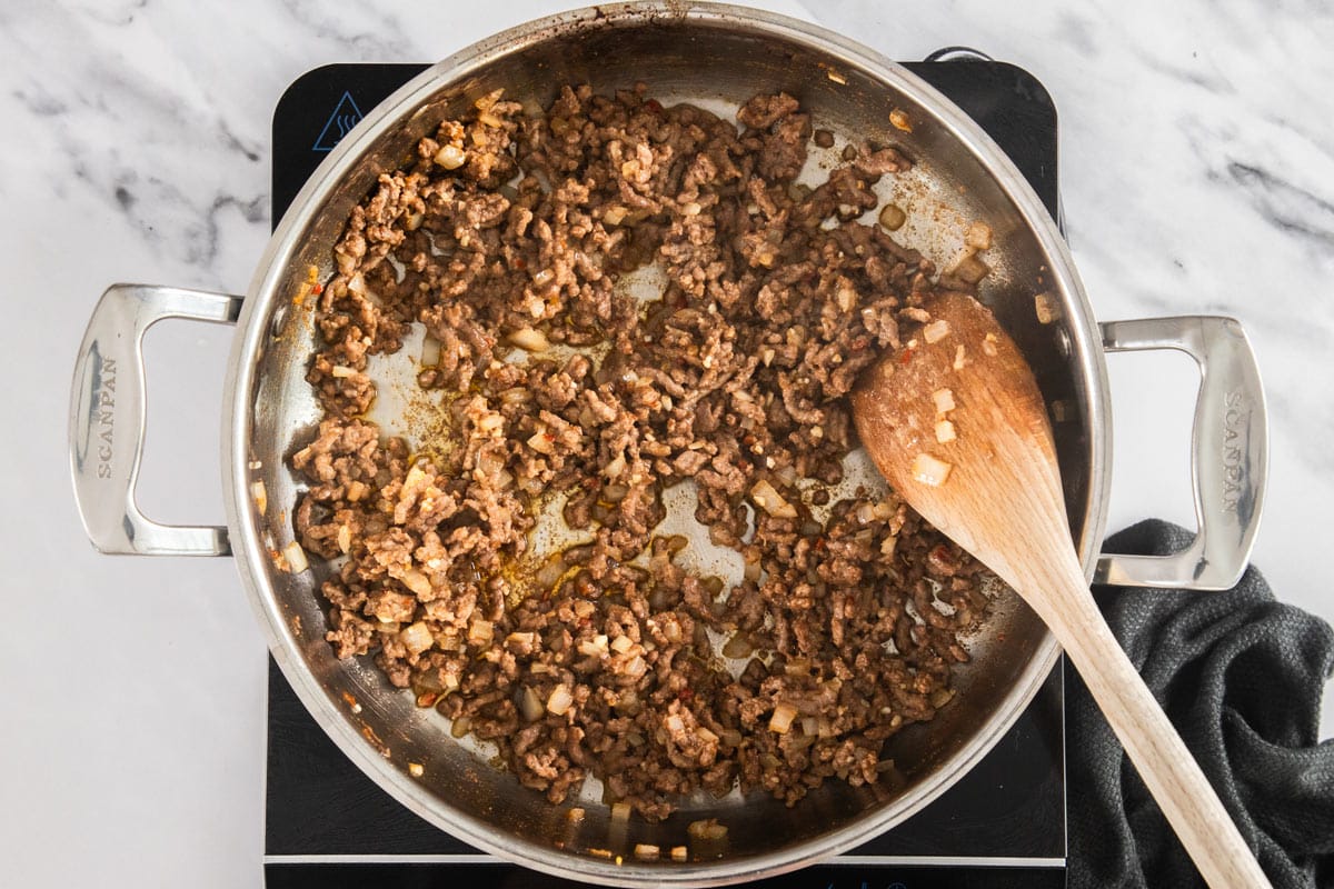 hamburger being browned in a skillet with a wooden spoon.