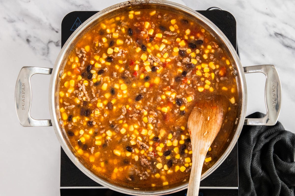 ingredients being cooked in an enchilada sauce in a skillet.