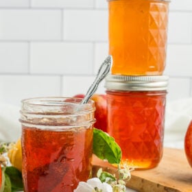three jars of apple jelly with a small branch of apple tree blossoms.