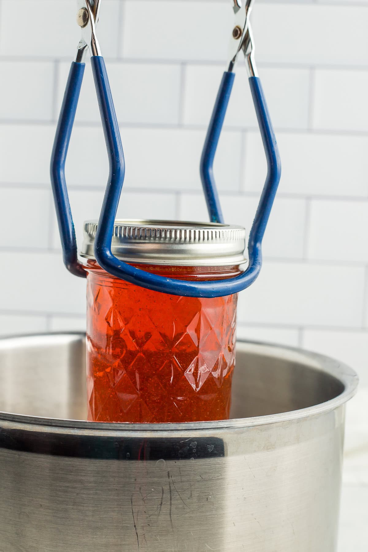 canning tongs holding a jar over a canning pot.