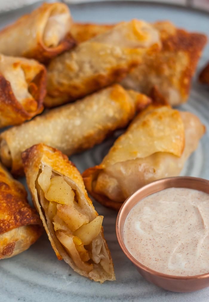 a stack of apple pie air fryer egg rolls with a small bowl of spiced yogurt.