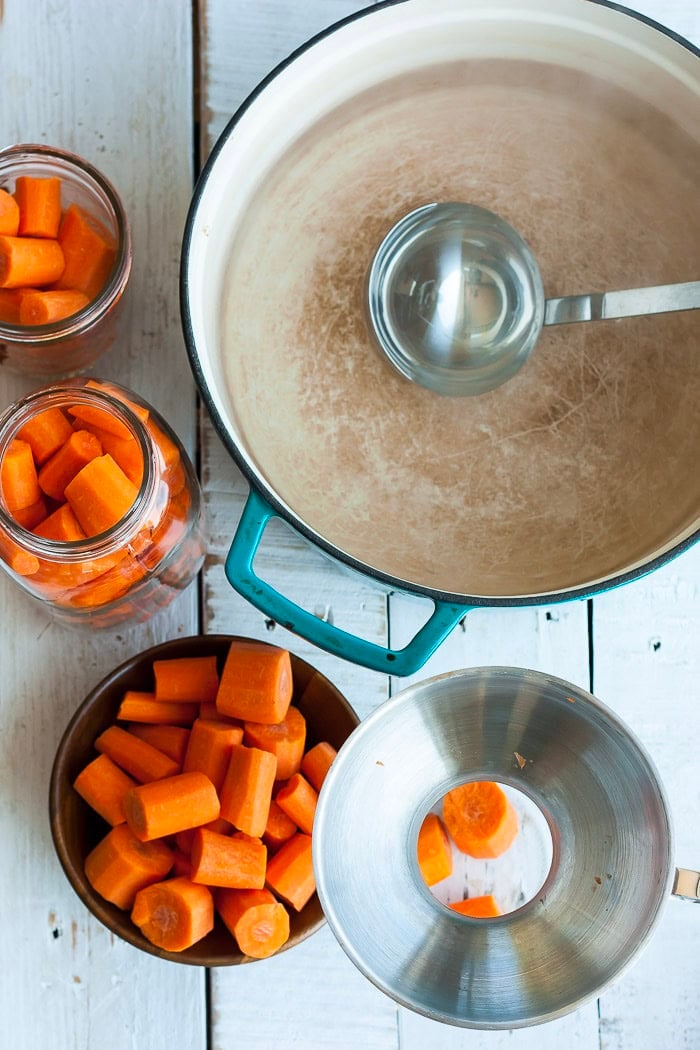 a canning funnel in a jar with bowls of carrots and a Dutch oven.