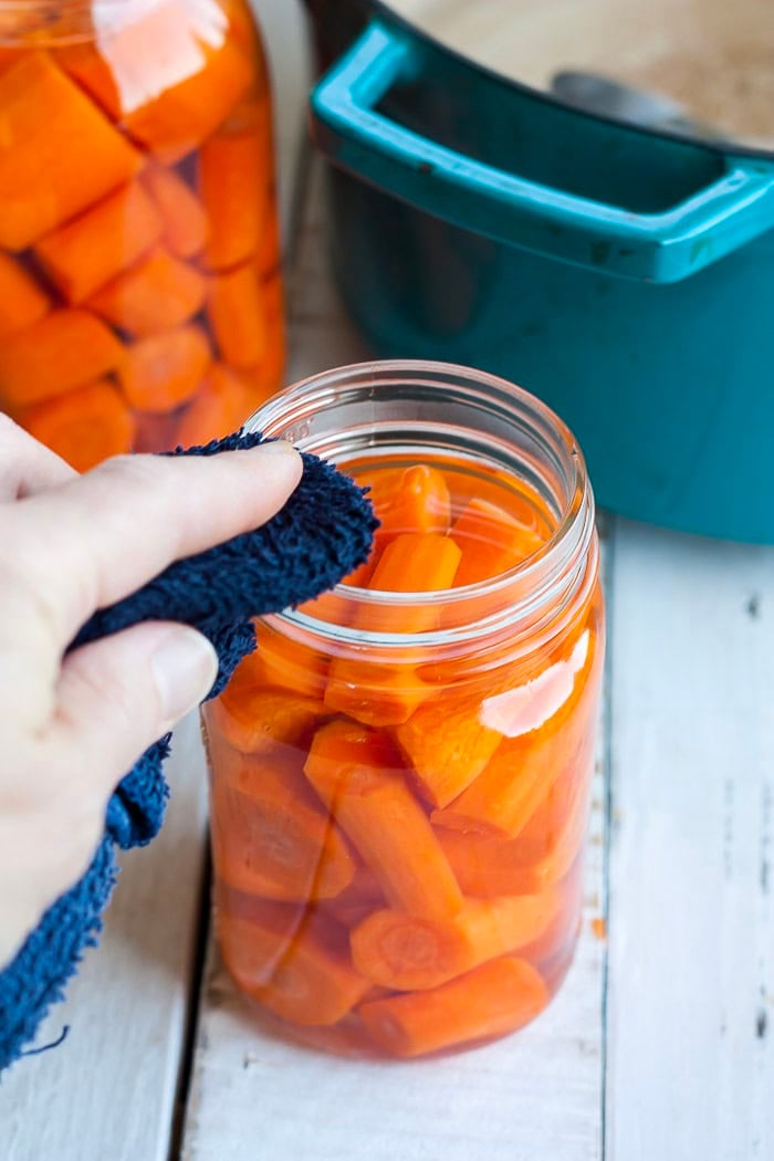 a blue rag wiping the rim of a jar.