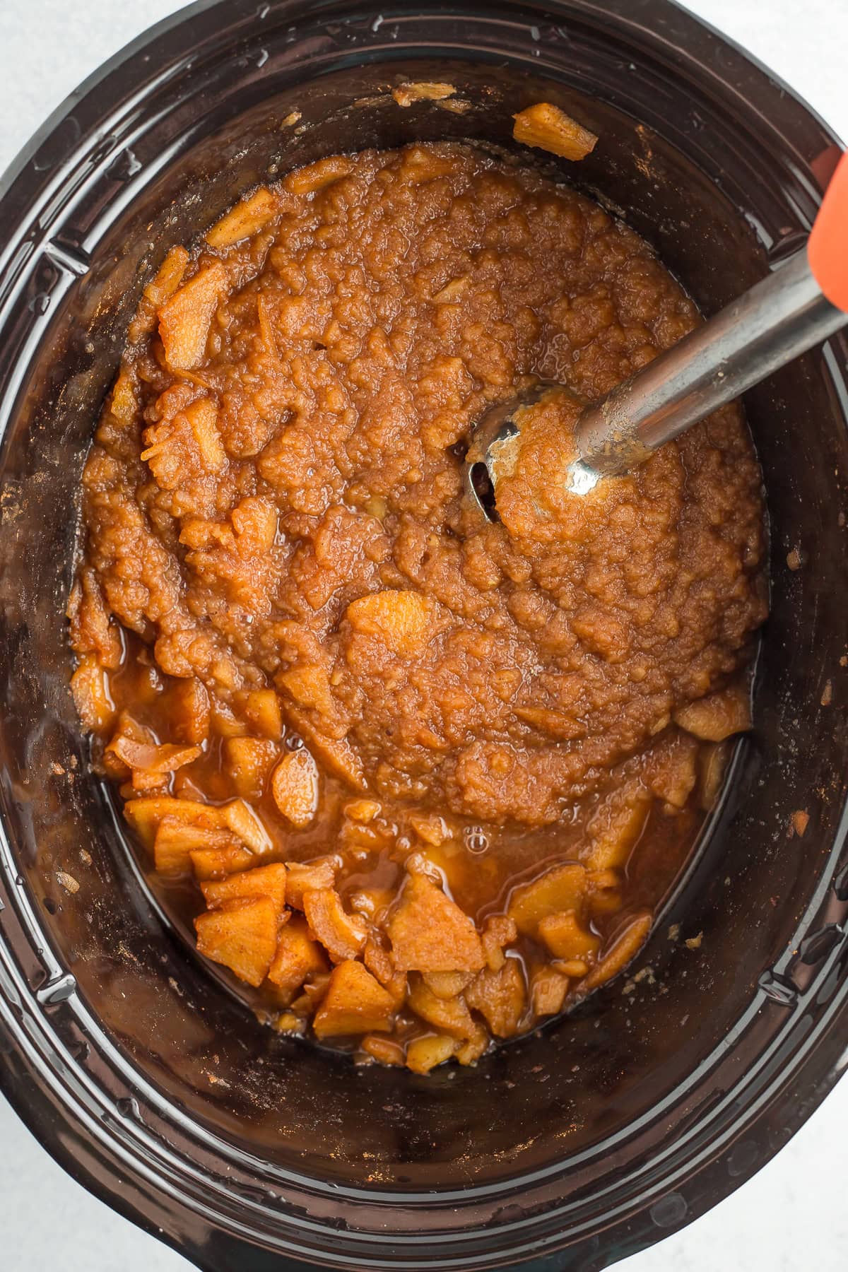 an immersion blender blending fruit in a crockpot.