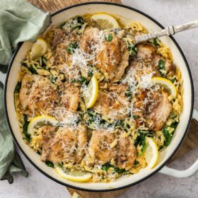a white and black skillet with orzo and chicken, slices or lemon, spinach, and Parmesan.