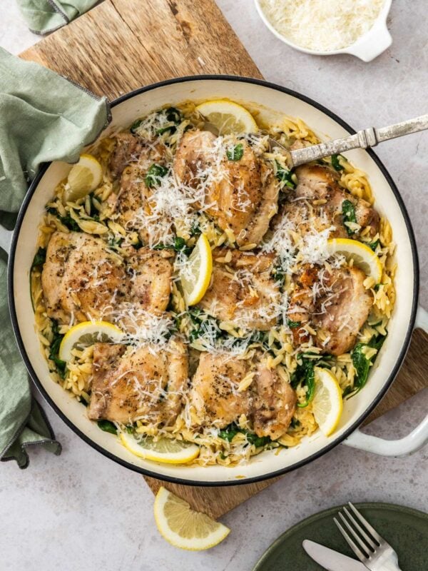 a white and black skillet with orzo and chicken, slices or lemon, spinach, and Parmesan.