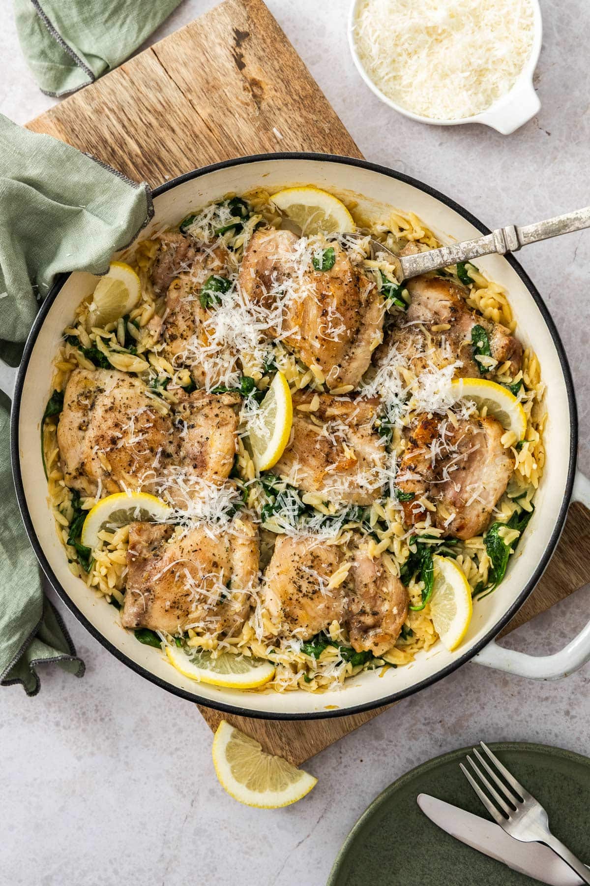 a white and black skillet with orzo and chicken, slices or lemon, spinach, and Parmesan.