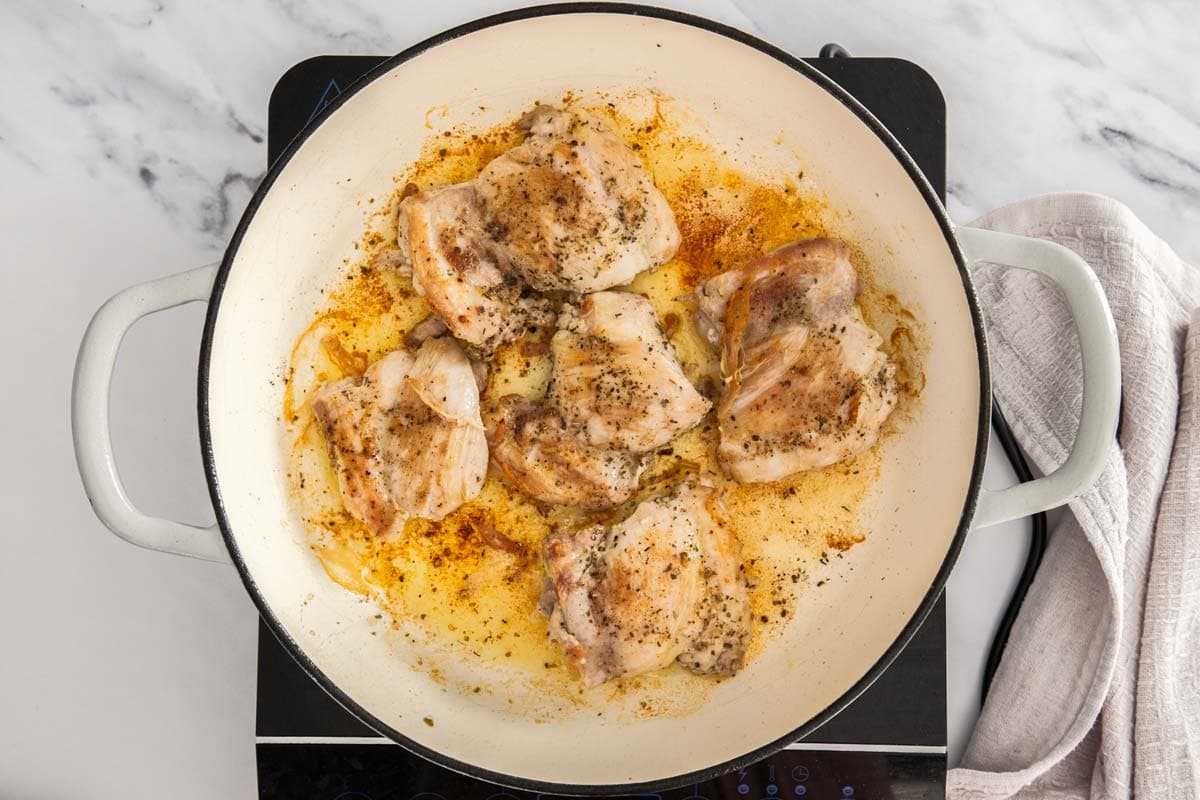 chicken being browned in a white skillet with olive oil.