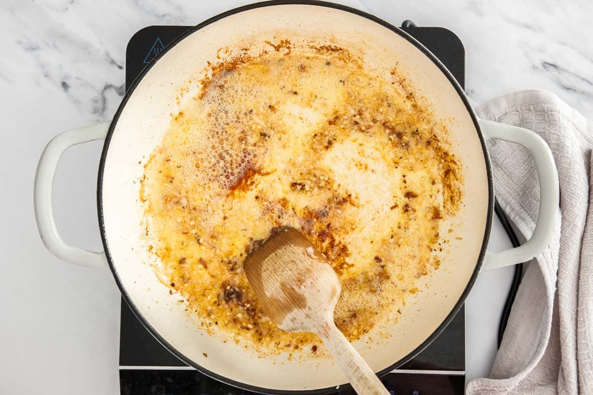 garlic and shallots being browned in a white skillet.