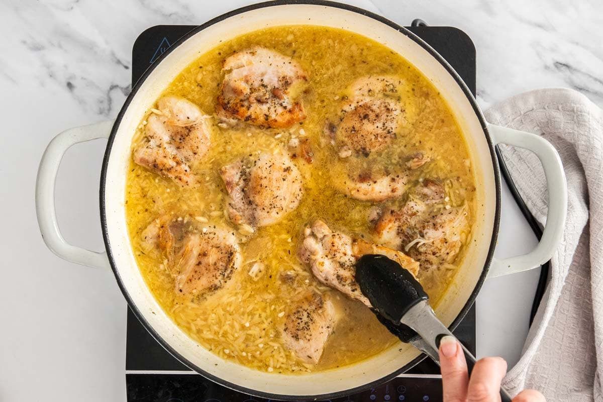 tongs place chicken in a white skillet with pasta.
