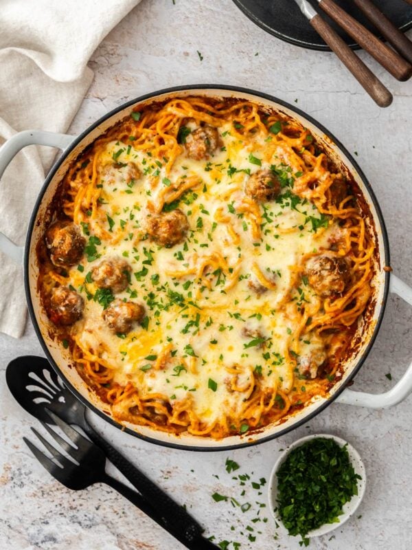 spaghetti and meatball casserole in a white skillet topped with chopped parsley.