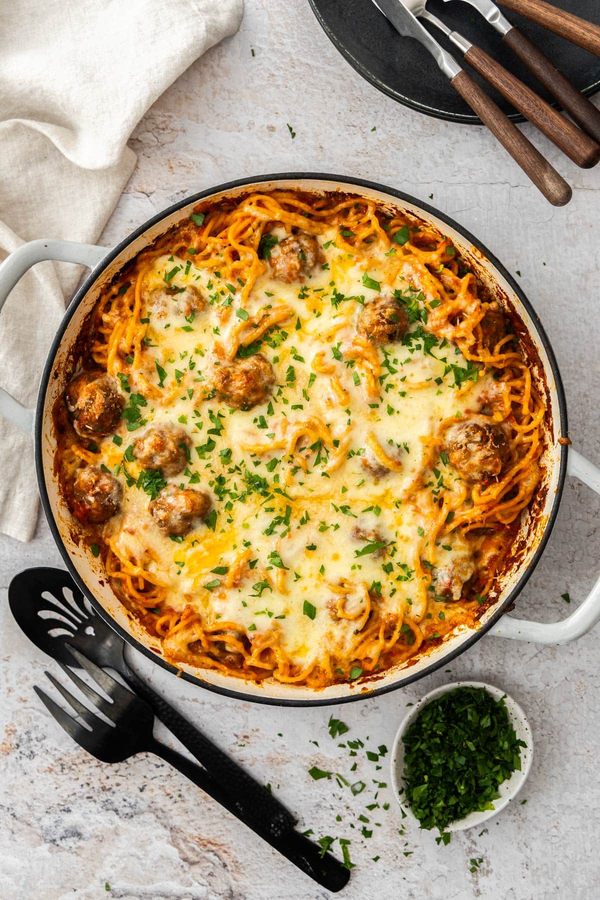 spaghetti and meatball casserole in a white skillet topped with chopped parsley.