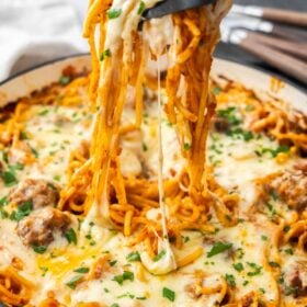 a fork and spoon with a serving of noodles hovering over a pot of casserole.