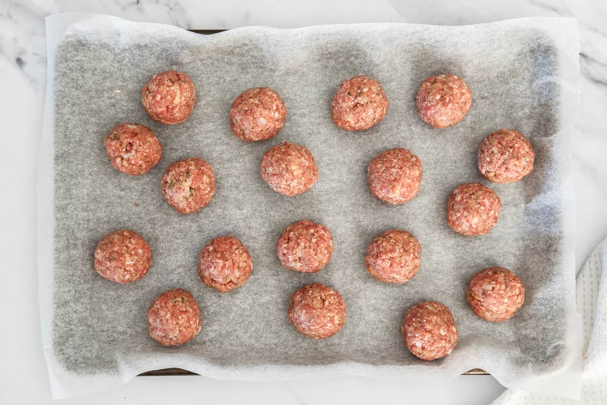 uncooked meatballs on a baking sheet lined with parchment.