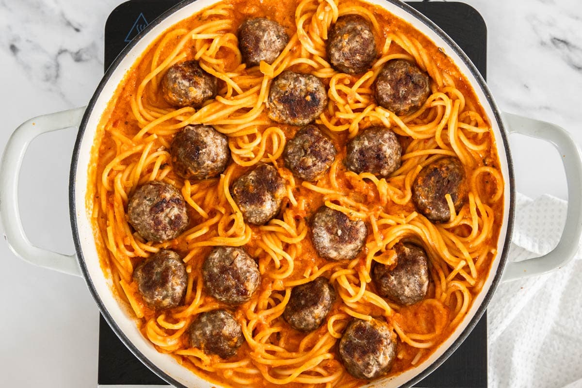 noodles and meatballs in sauce in a white skillet.