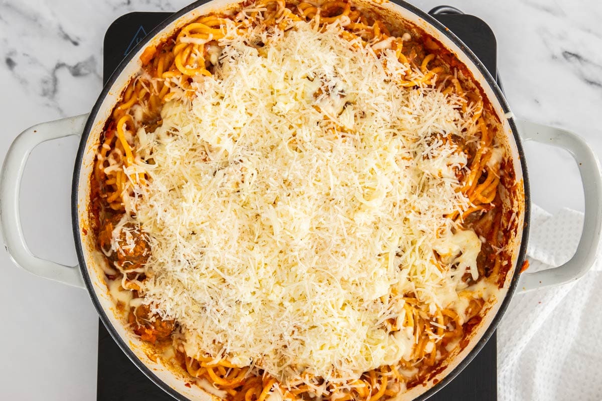 cheese on top of a pasta casserole in a white skillet.