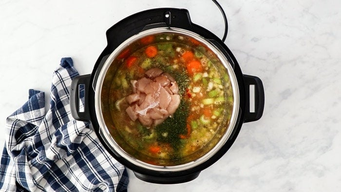 uncooked chicken breasts and broth added to a pressure cooker.