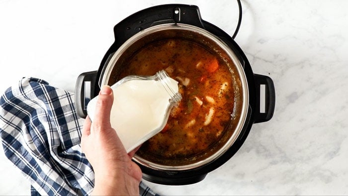 a bottle of heavy cream being poured into a pressure cooker.