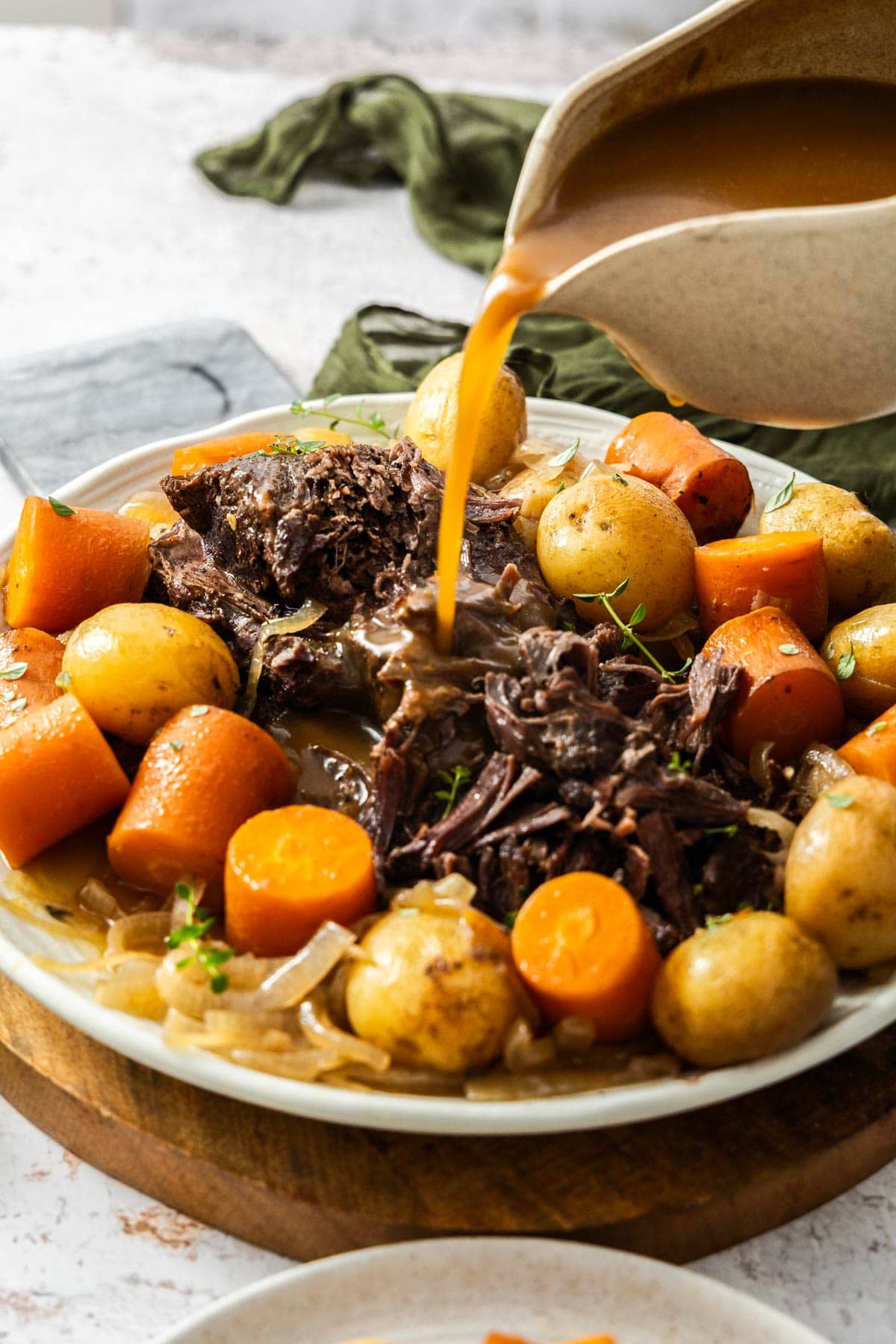 a gravy boat pouring gravy over a plate of shredded beef.