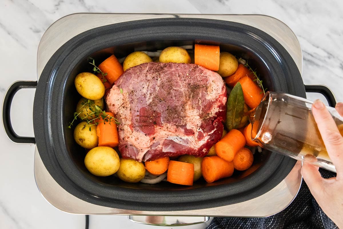 a cup of beef broth being poured into a crockpot.
