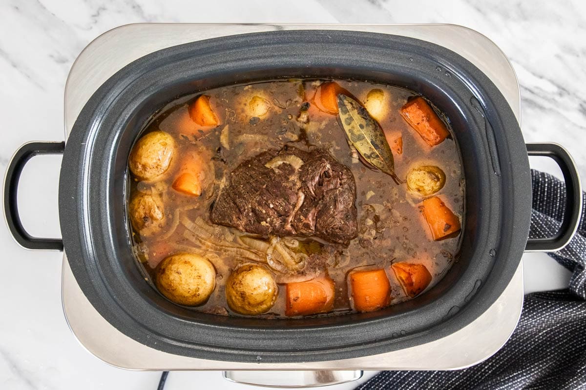 a cooked roast and veggies in a crockpot with a bay leaf.